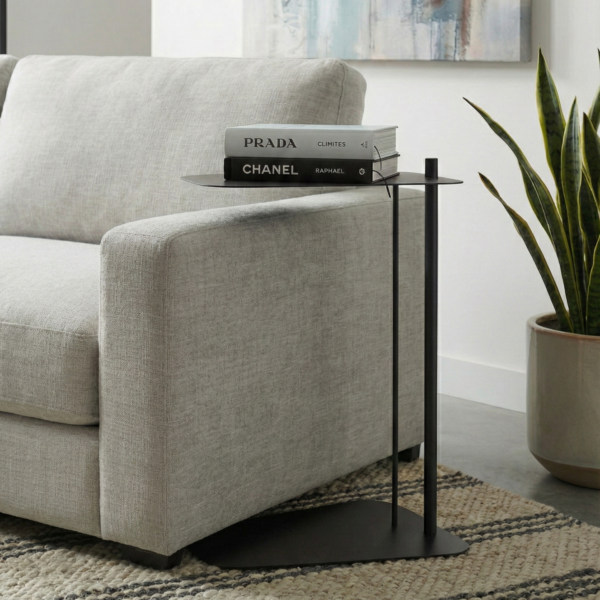 Czarny metalowy stolik boczny pomocniczy do kanapy LEAF w nowoczesnym salonie. Minimalistyczny stolik typu C wsunięty pod narożnik, z książkami na blacie.